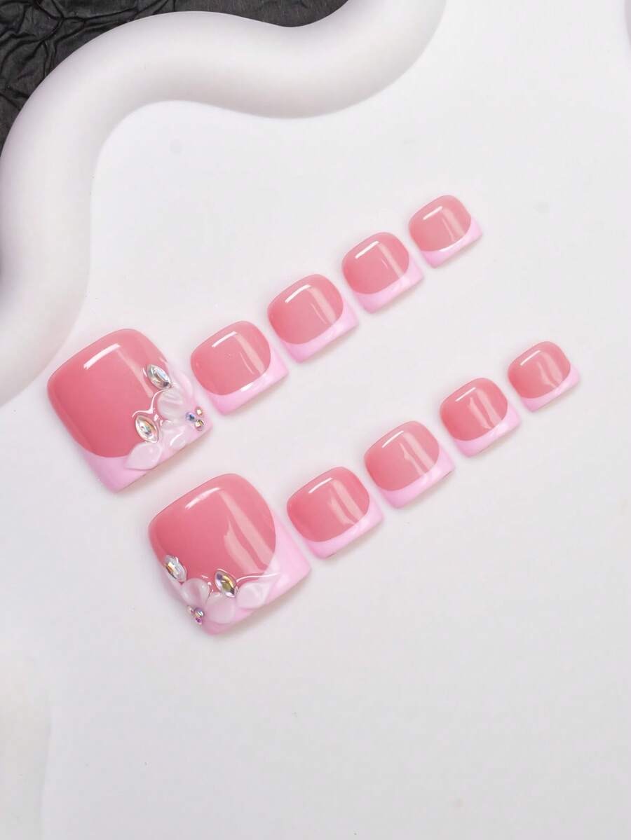 Pink French tip press-on toenails shown at an angle on a white surface