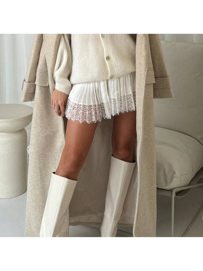 Cream lace mini skirt styled with a knit coat and tall boots