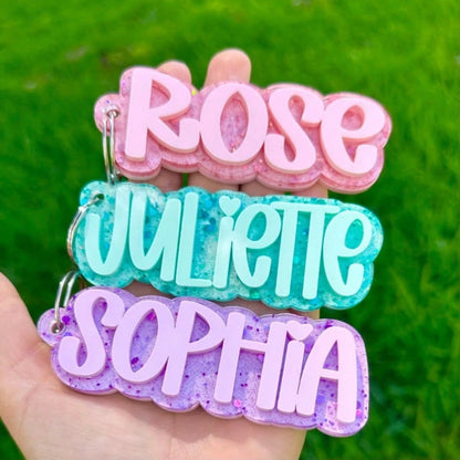 Three personalized glitter name keychains held in hand