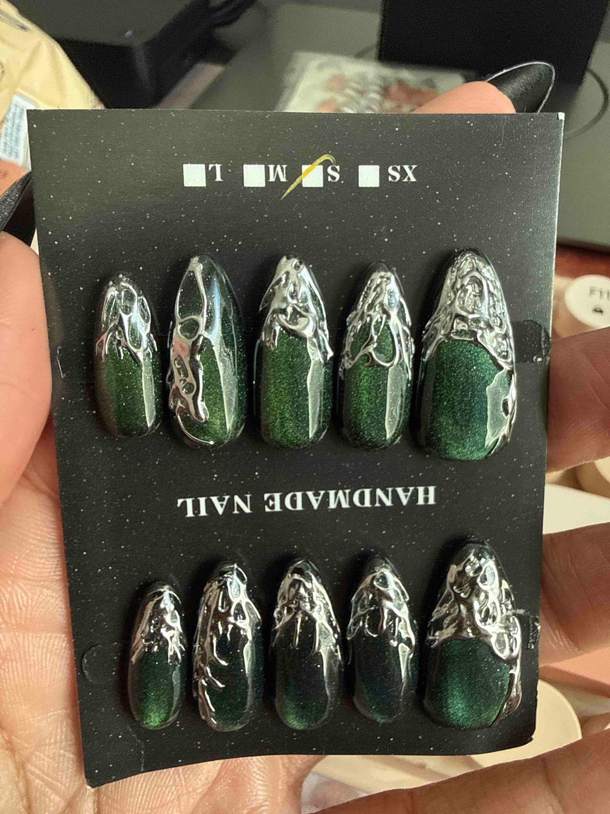 Emerald and silver chrome almond press-on nails on their card