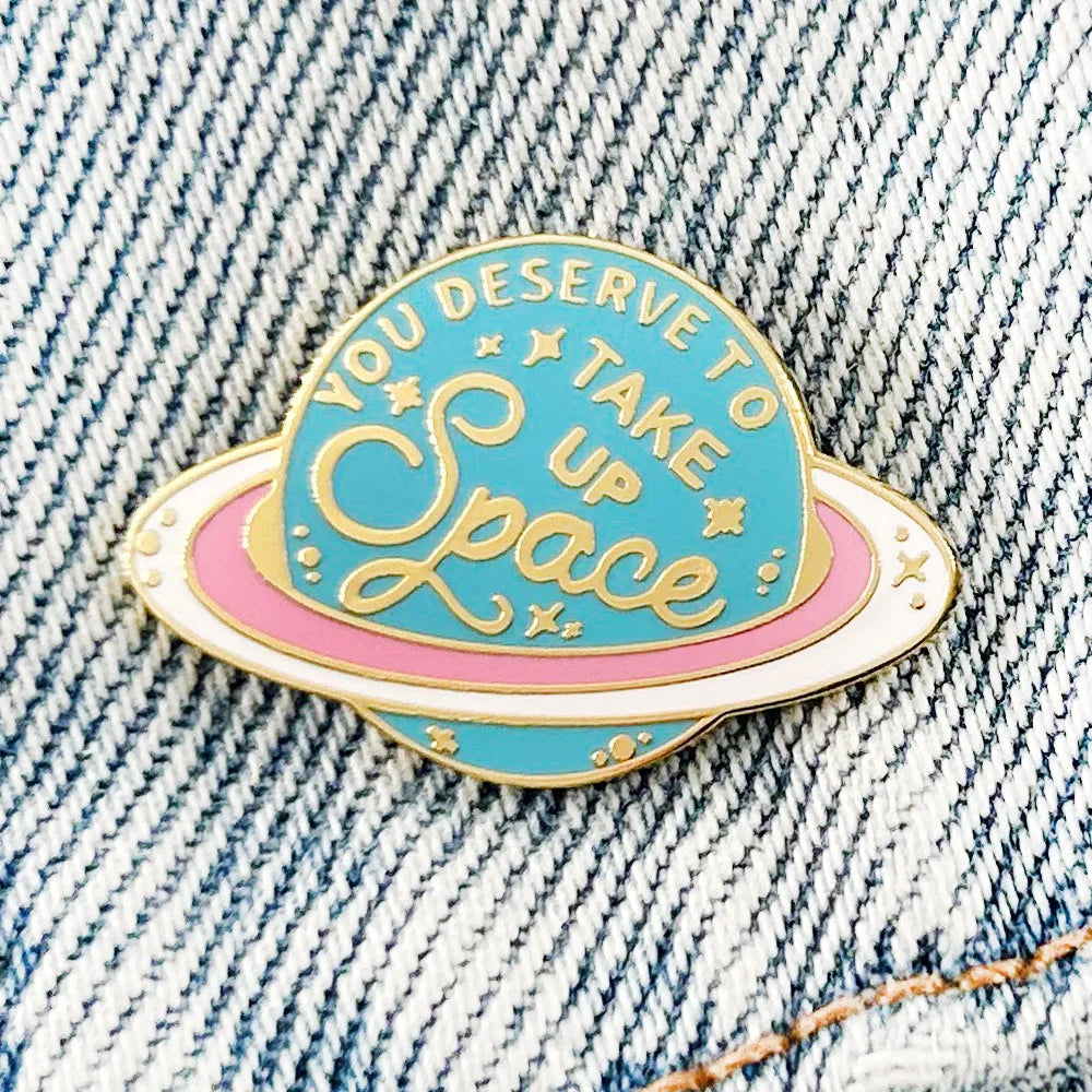 Take Up Space Saturn enamel pin on denim