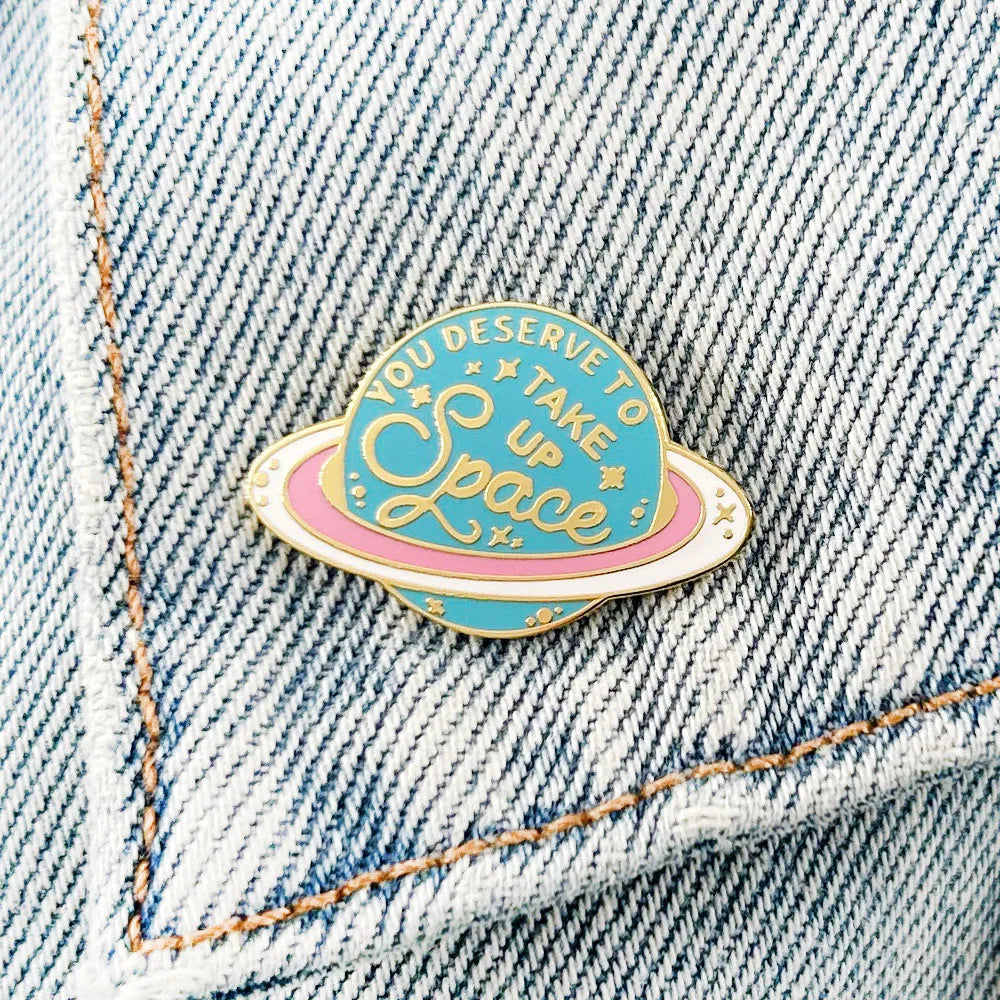 Saturn enamel pin pinned to a denim jacket pocket