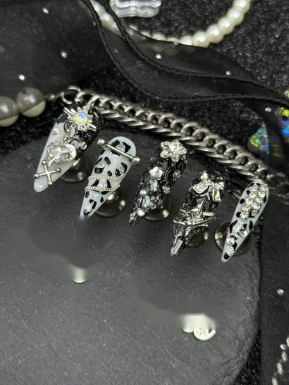 Long stiletto press-on nails in black and white cow print with silver crosses and crystals