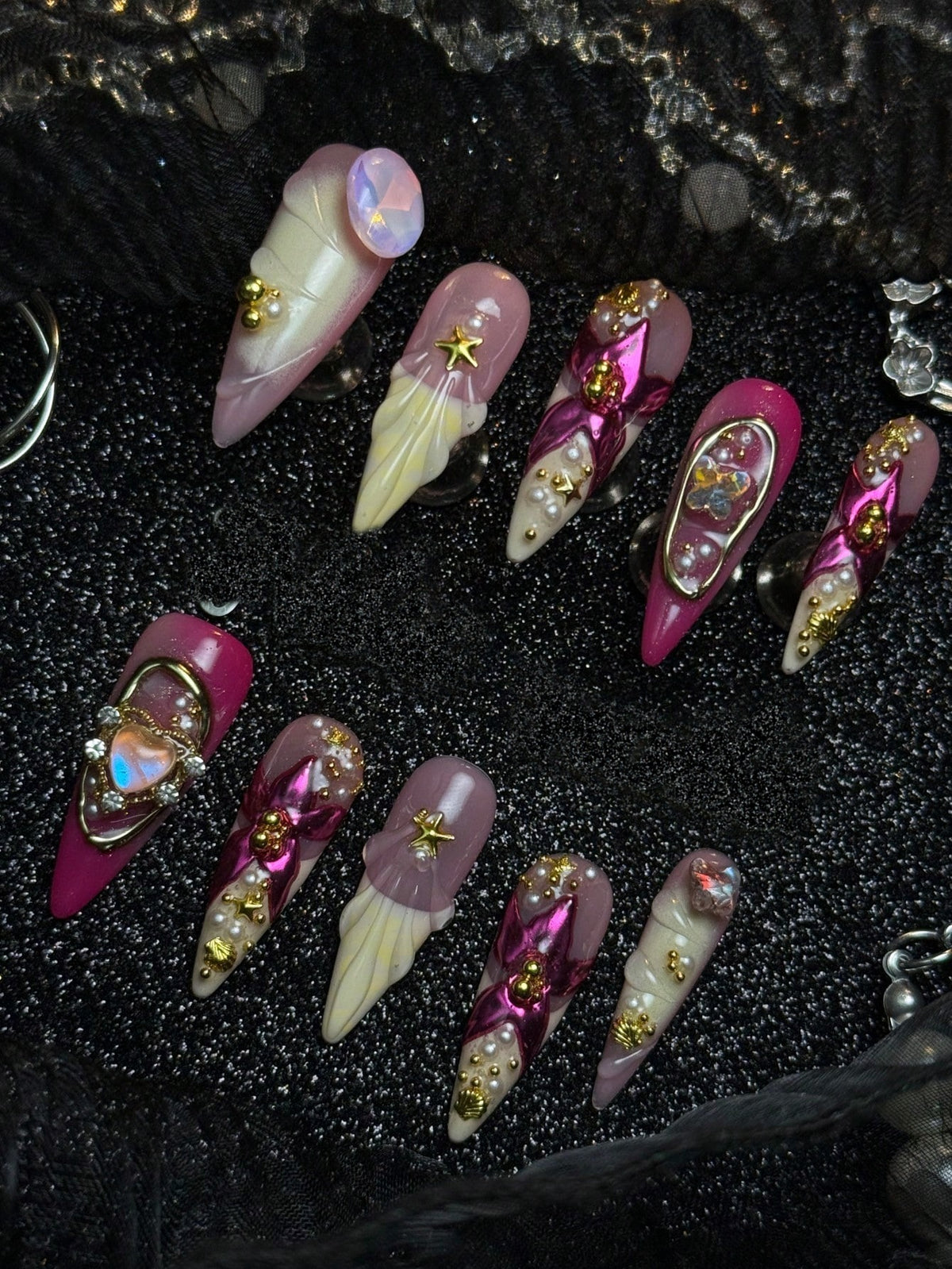Hot pink chrome and pearl stiletto press-on nails laid out in two rows