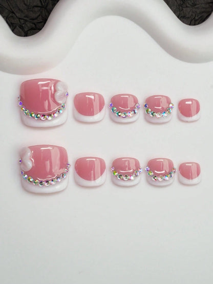 Short square pink French press-on toenails with iridescent crystals and a 3D bow, flat lay